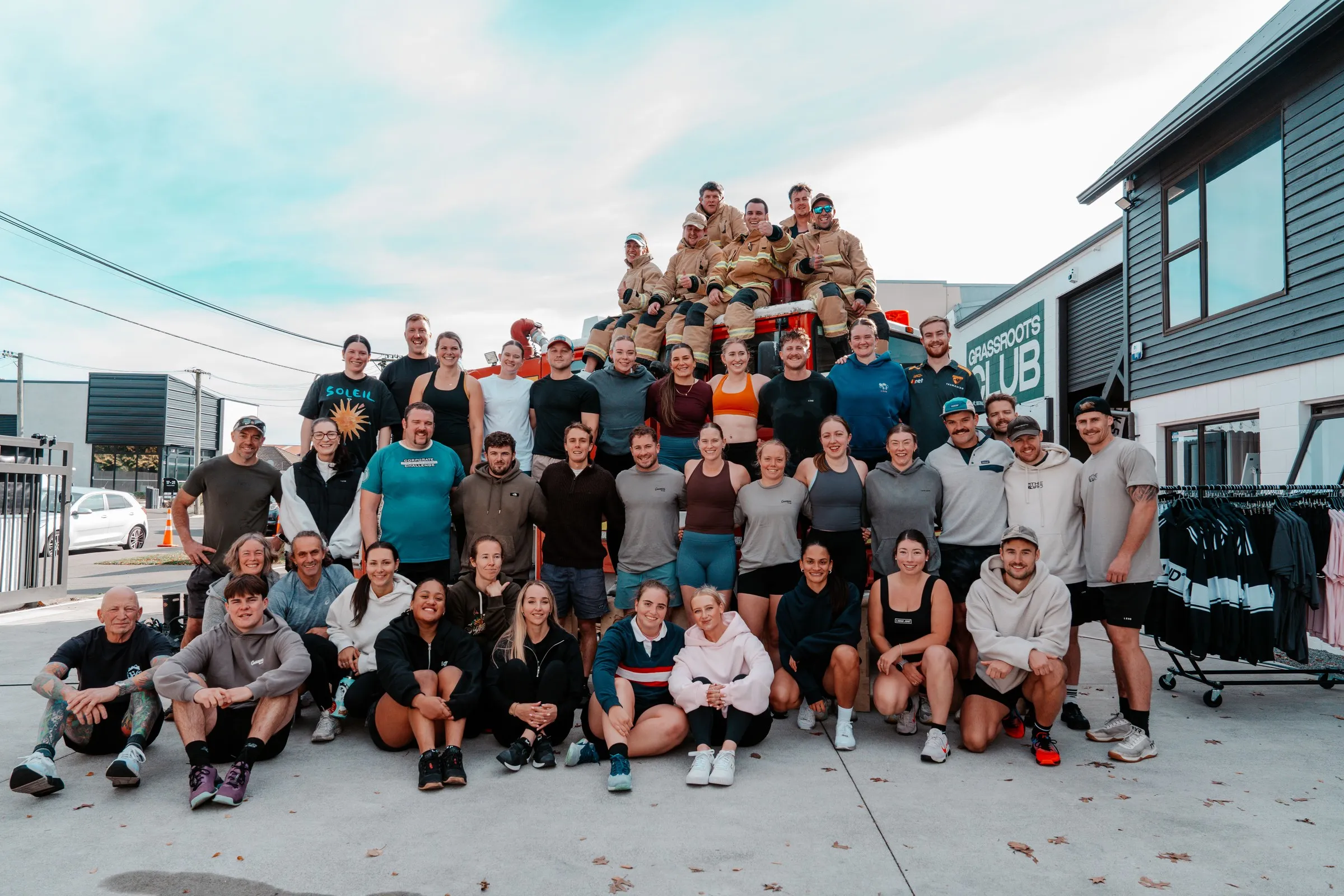 The whole club outside the gym — firefighters in full kit up on the fire truck behind the crew.