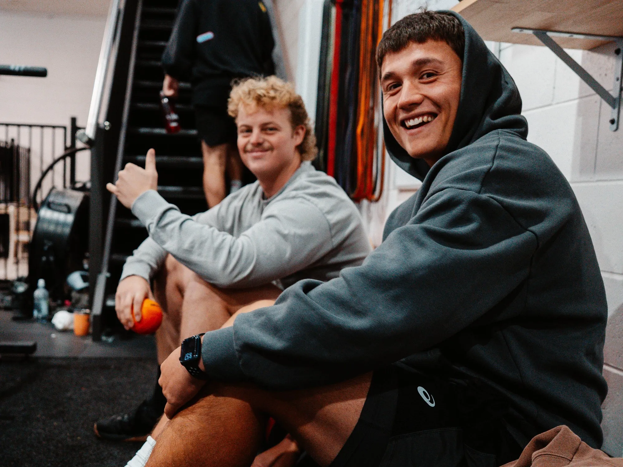 Two members relaxing on the floor after a session, all smiles and a thumbs up.
