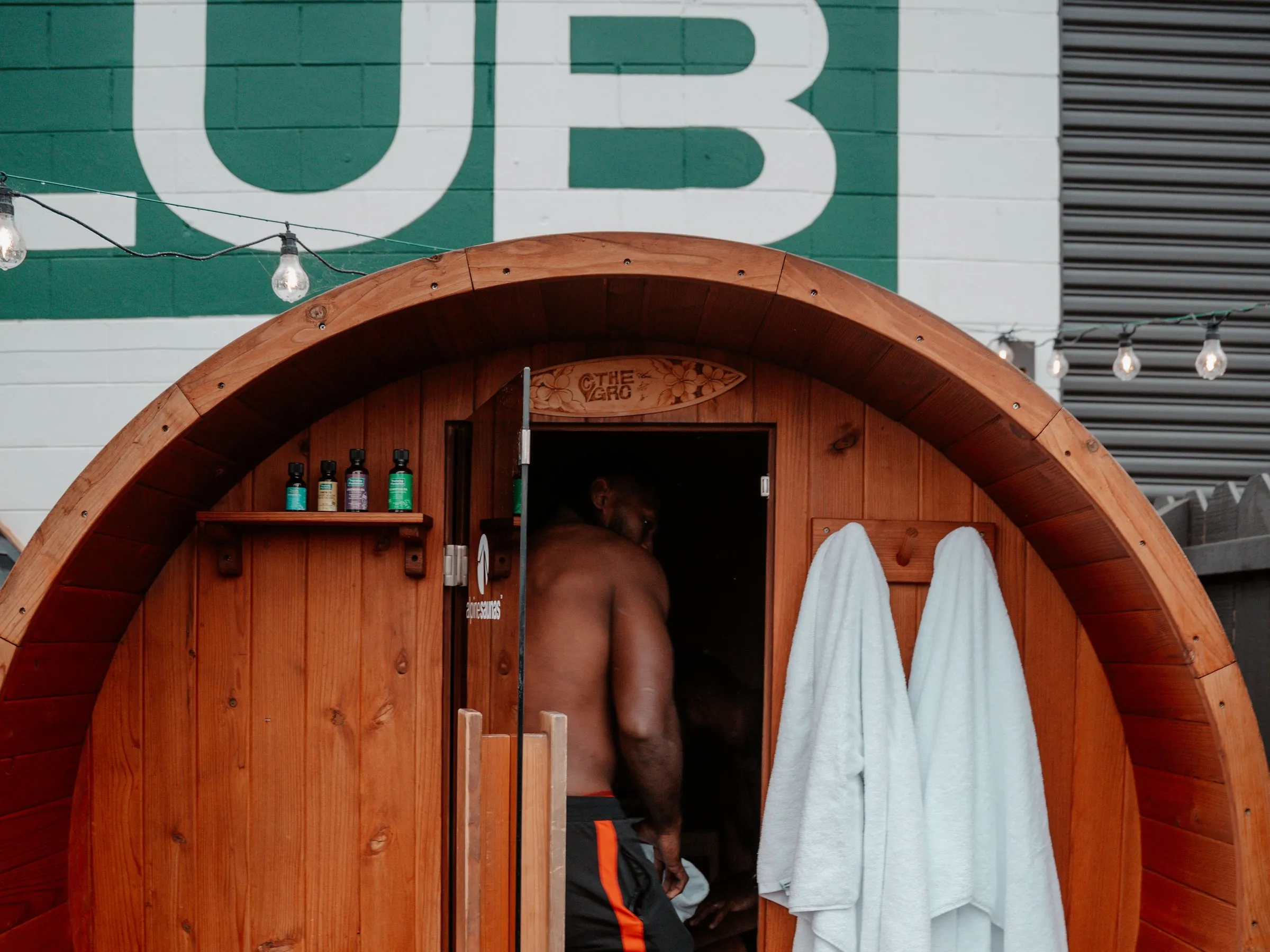 The barrel sauna with the door open, under the big Grassroots Club wall.