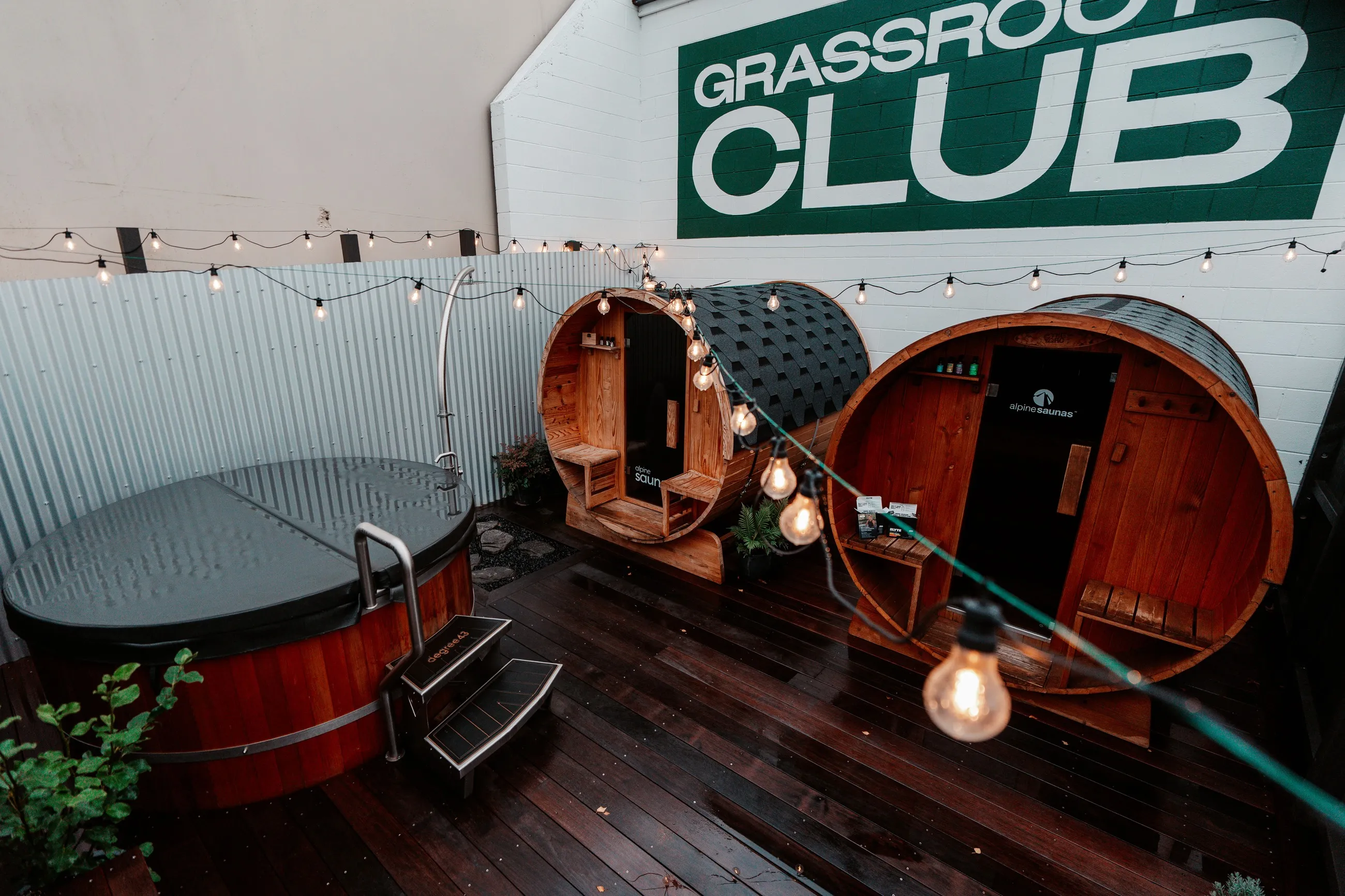 The full recovery deck — cold plunge and two barrel saunas under festoon lights.